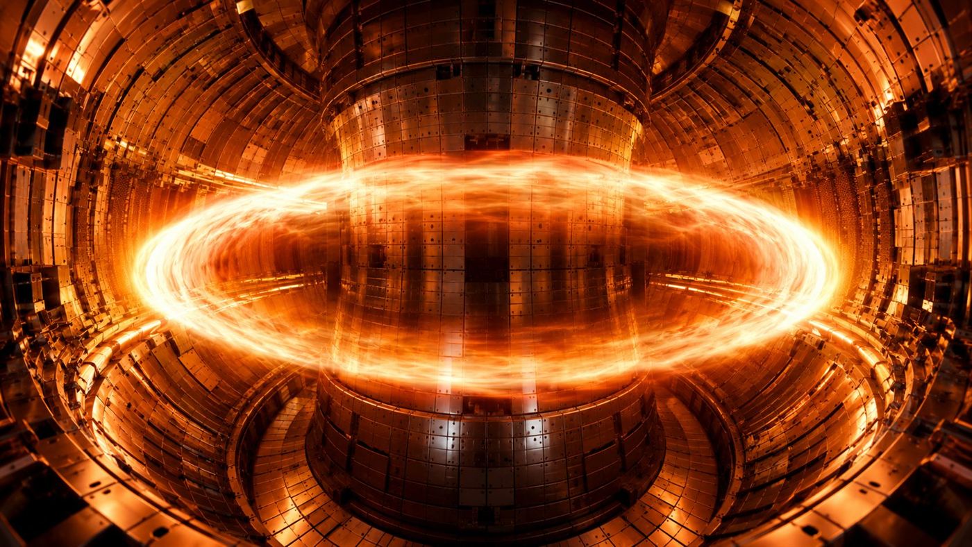 The glowing interior of a doughnut-shaped tokamak fusion reactor with a ring of superheated orange plasma swirling inside the metal vessel