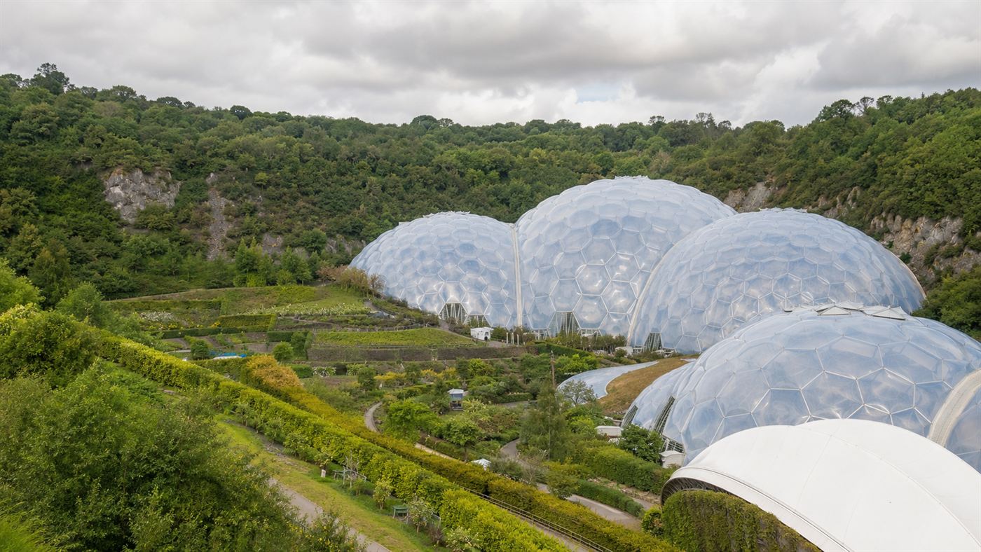 The Eden Project's huge white geodesic bubble domes nestled in a green reclaimed clay crater in Cornwall under a bright sky