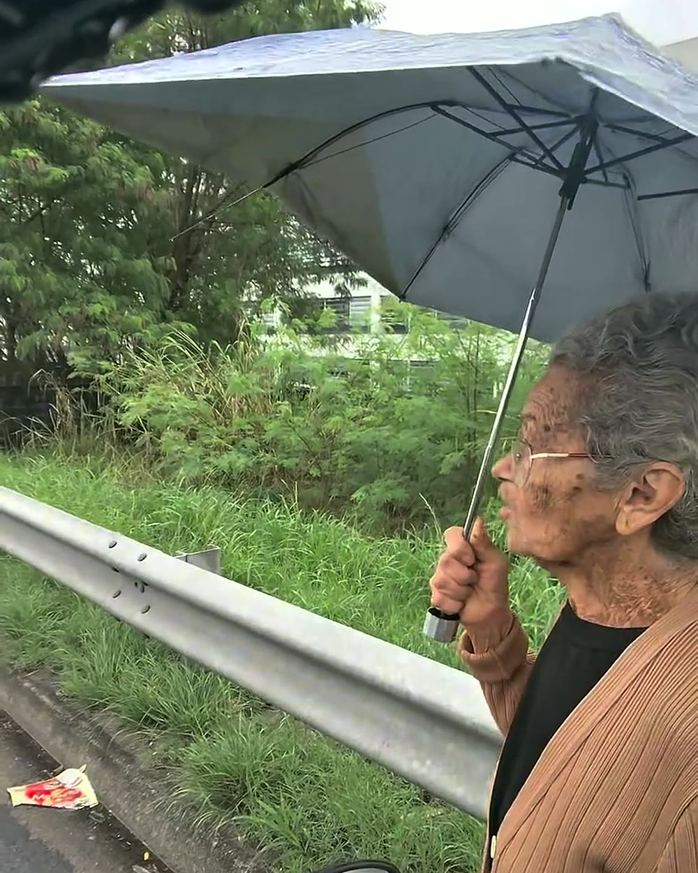 Idosa de 89 anos parada no acostamento da Linha Vermelha com um guarda-chuva aberto, flagrada pela câmera do motociclista