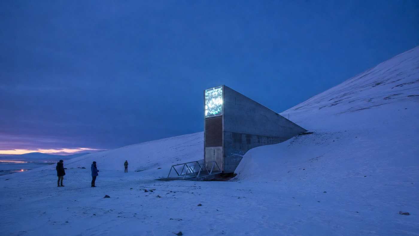 The wedge-shaped concrete entrance of the Svalbard Global Seed Vault jutting from a snow-covered Arctic mountainside under a deep blue polar twilight