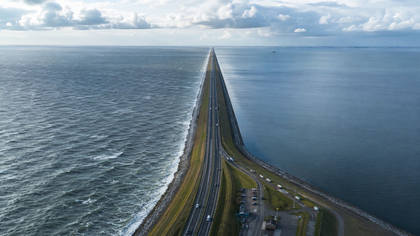The long straight Afsluitdijk dam stretching to the horizon across the water with a road and the sea on one side and a calm lake on the other