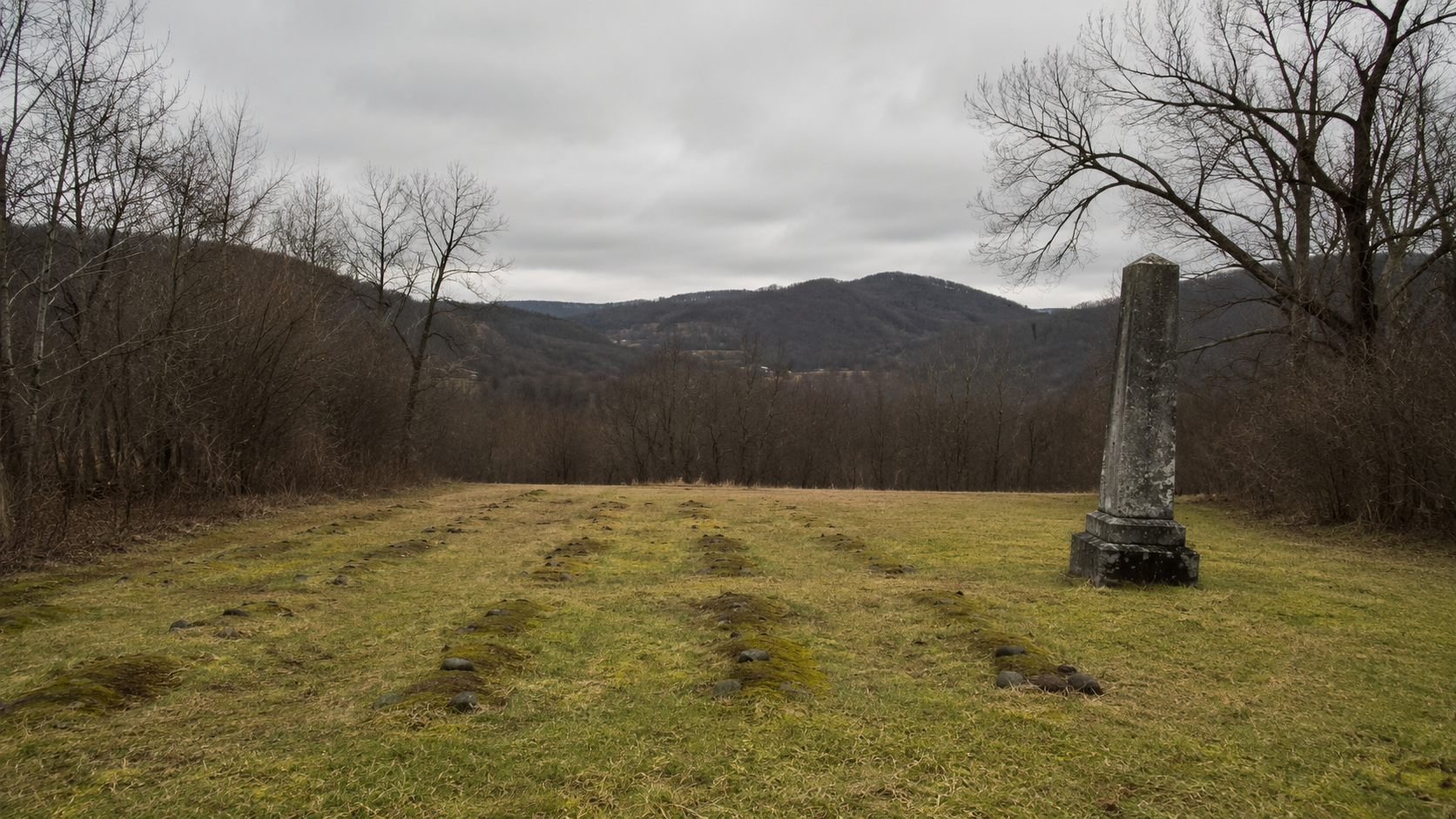 Rows of unmarked graves and a weathered stone memorial in a West Virginia field commemorating Hawks Nest Tunnel disaster victims