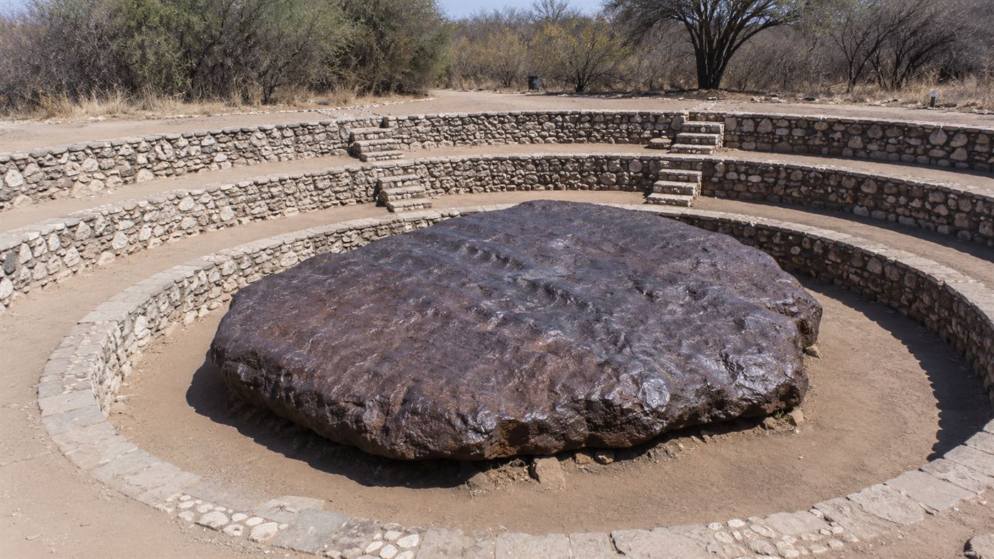 The huge flat dark slab of the Hoba meteorite sitting in a stone amphitheatre in the Namibian bush