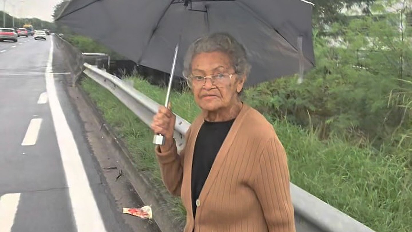 Idosa perdida na Linha Vermelha andando pelo acostamento com guarda-chuva, em frame do vídeo viral