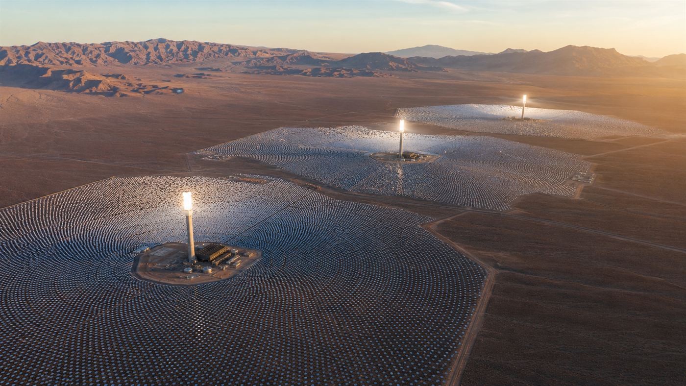 Ivanpah solar plant heliostats in the Mojave Desert with three tall power towers glowing with concentrated sunlight at dawn