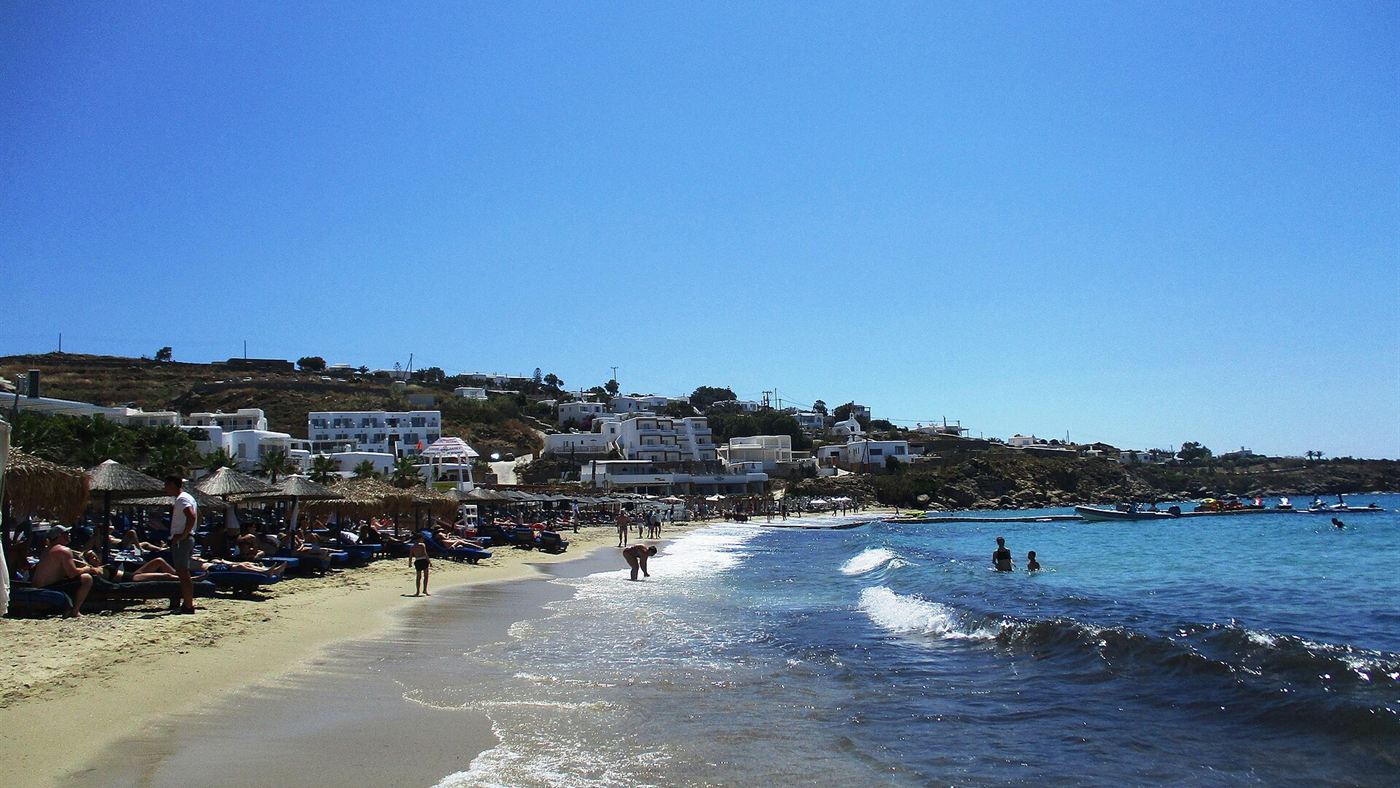 Praia grega de mar azul-turquesa, cenário parecido com o mostrado por Maisa nos stories da viagem