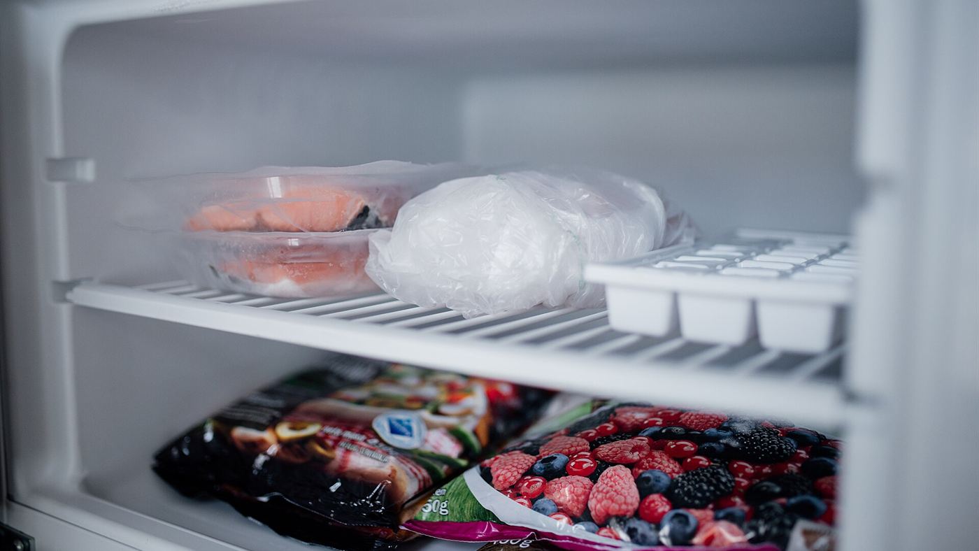 Comida congelada em sacos plásticos dentro do congelador, incluindo peixe e frutas vermelhas