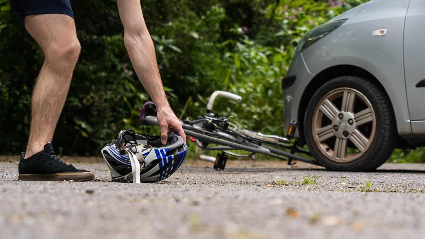 Ciclista caído no chão ao lado da bicicleta e de um carro após acidente de trânsito