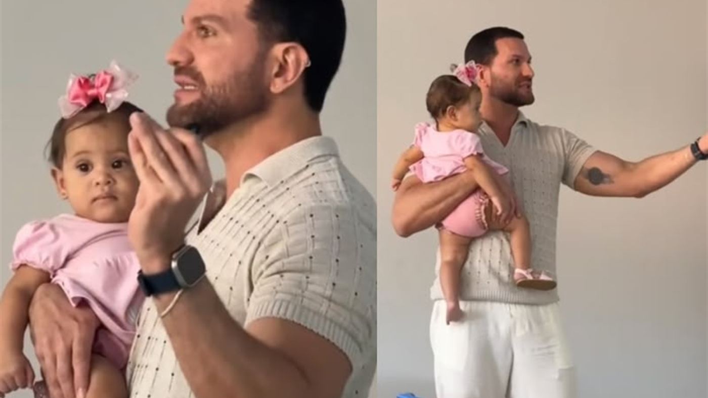 Professor Rodolpho Guedes sorri segurando a bebê Bárbara no colo