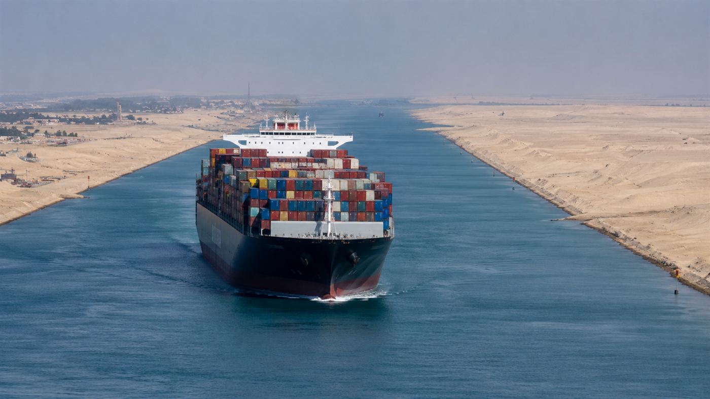 A large container ship moving through the Suez Canal flanked on both sides by open desert