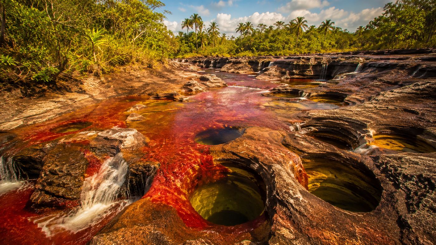 The colourful river flowing through ancient rock formations with small waterfalls and round potholes carved into the stone