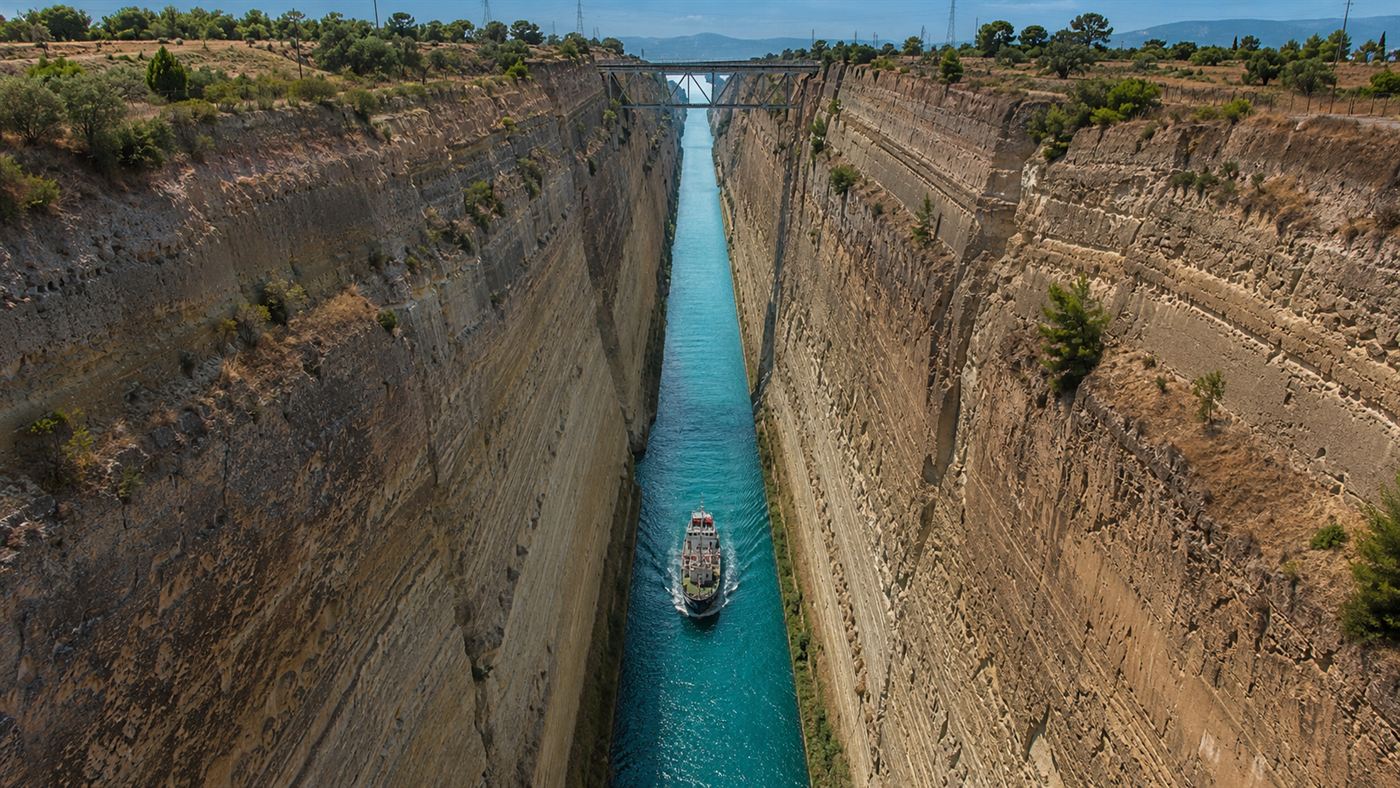 The narrow Corinth Canal cut deep between high vertical rock walls in Greece, a small ship passing through far below