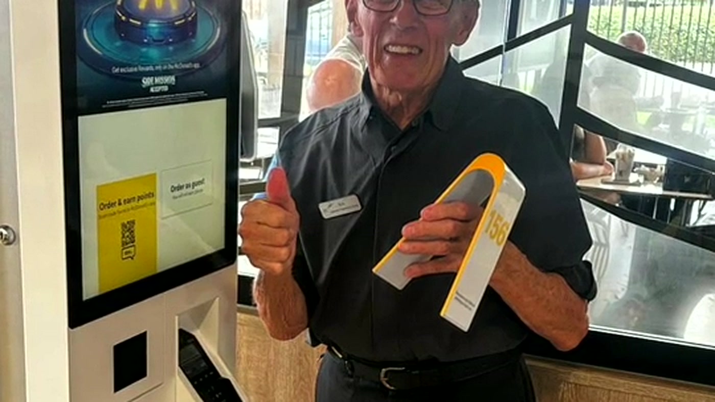 Eric Edwards, de 91 anos, faz sinal de positivo ao lado do totem de autoatendimento do McDonald's onde trabalha em Coventry