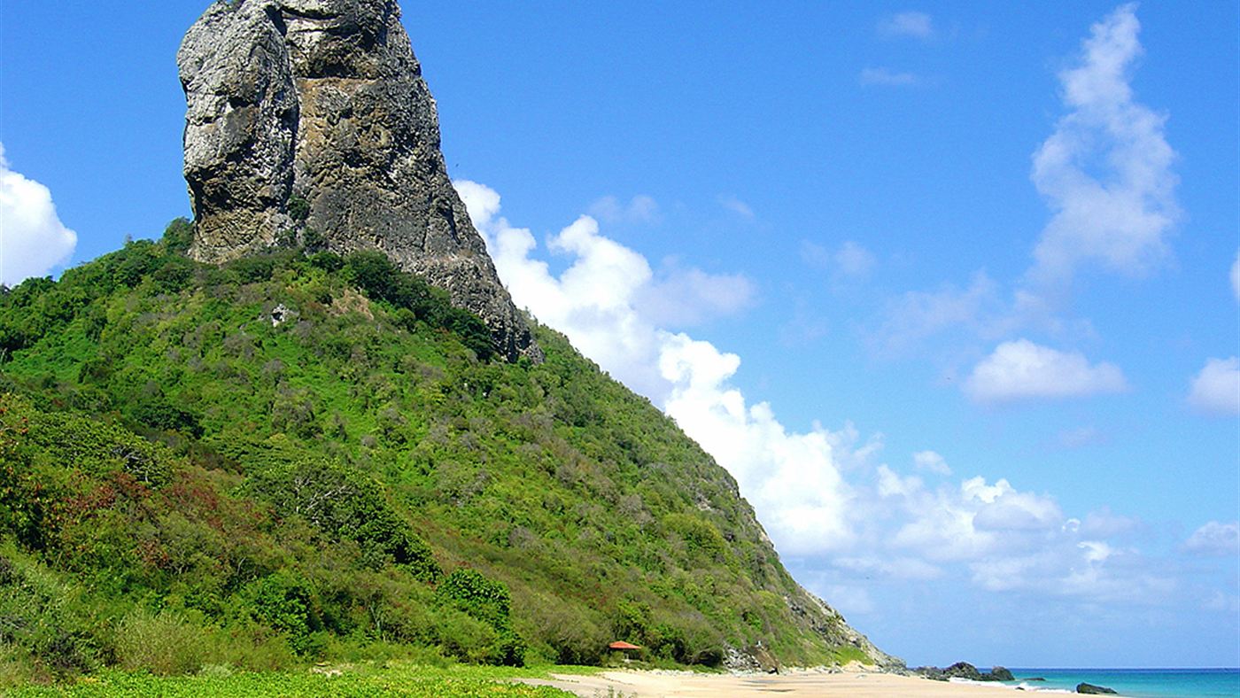O Morro do Pico visto da praia, com a base coberta de vegetação sobre a rocha vulcânica.