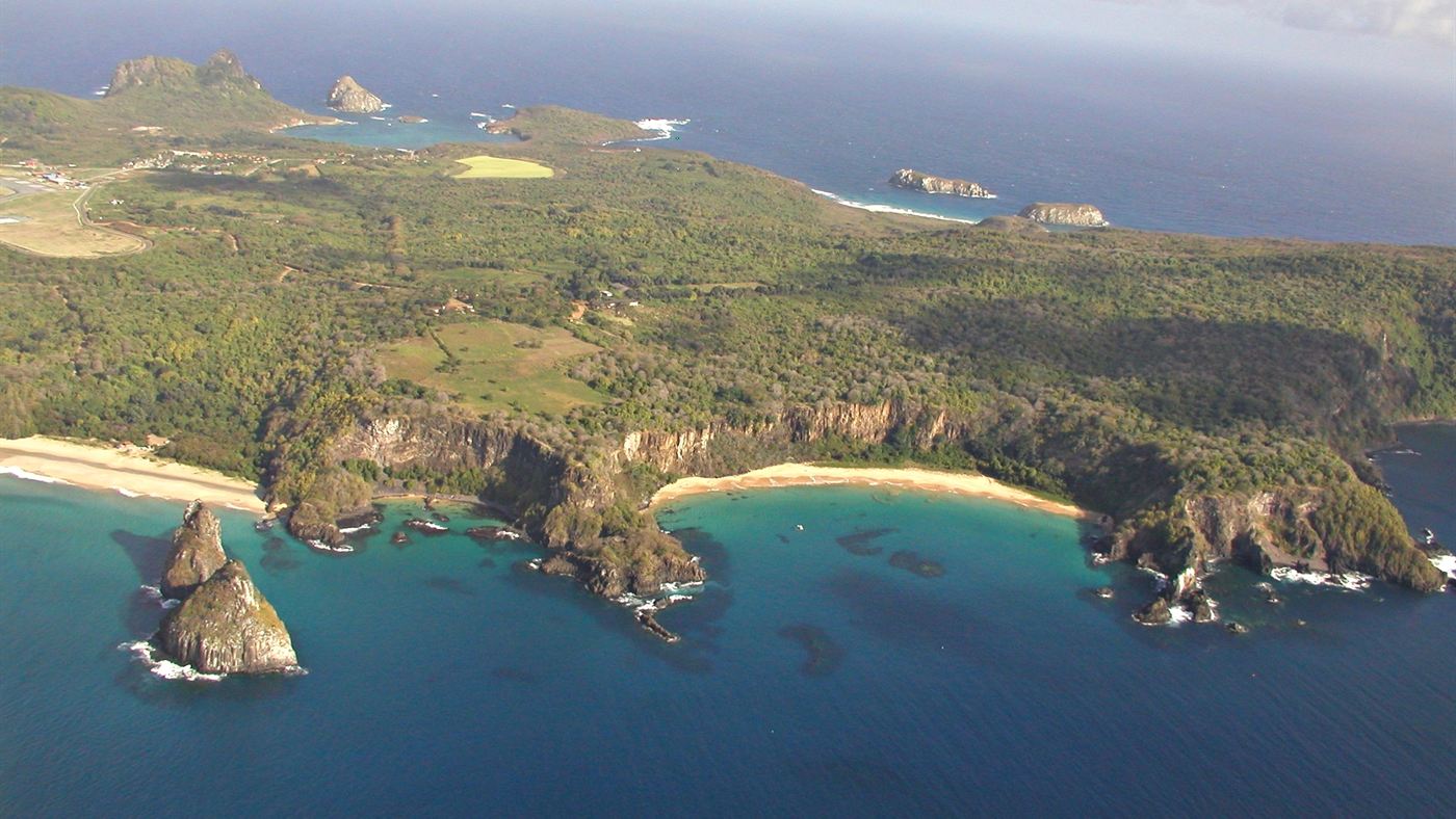 Vista aérea de Fernando de Noronha, com picos vulcânicos e enseadas ao longo da costa da ilha.