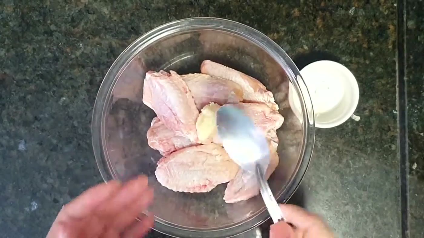 Pedaços de frango cru sendo temperados em uma tigela antes de ir à air fryer