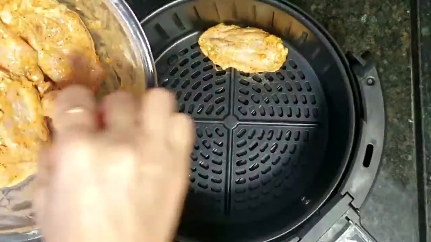 Pedaços de frango temperados sendo colocados no cesto perfurado da air fryer