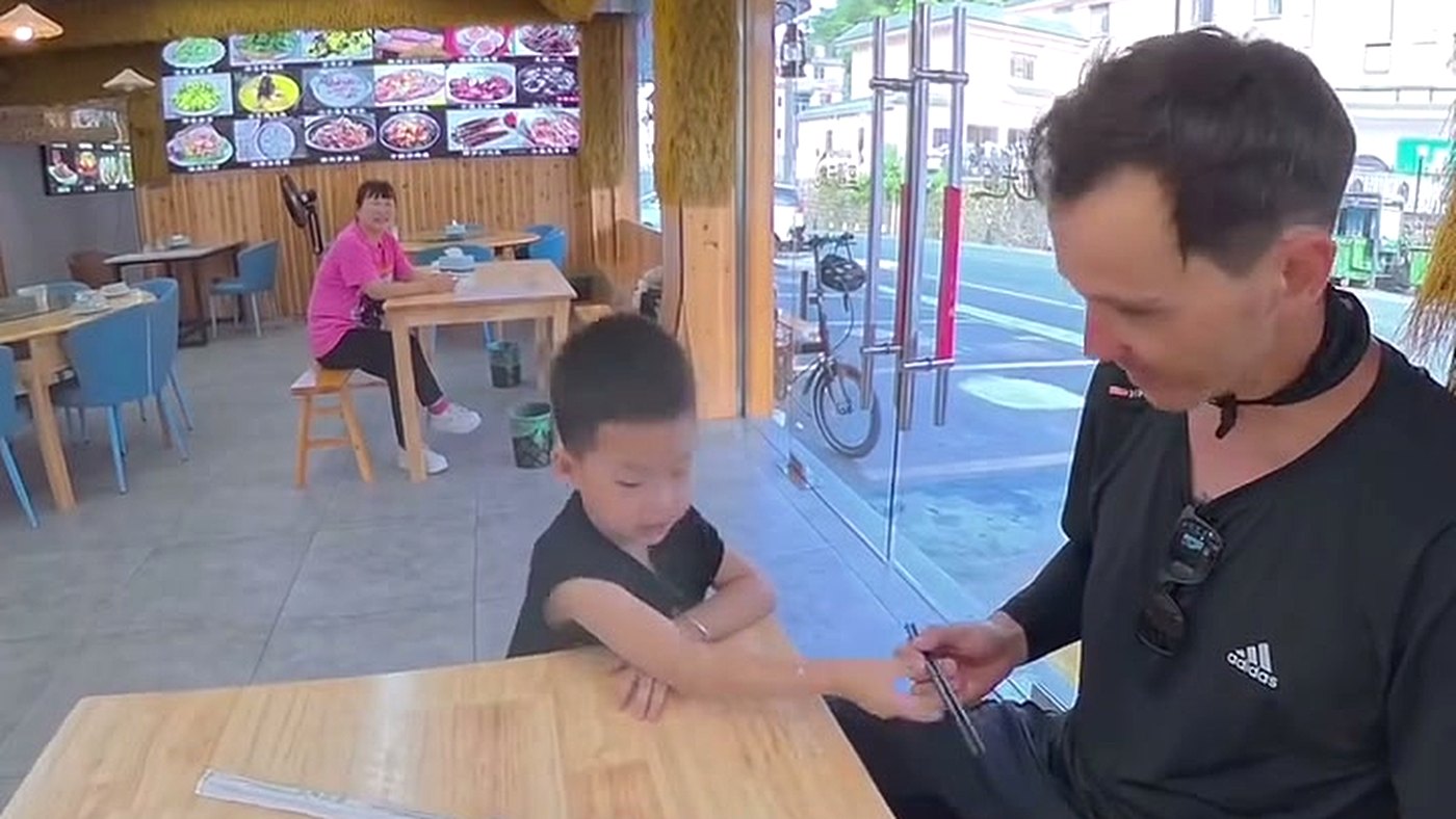 Menino chefe de restaurante para um ciclista na rua em Huangshan, na China