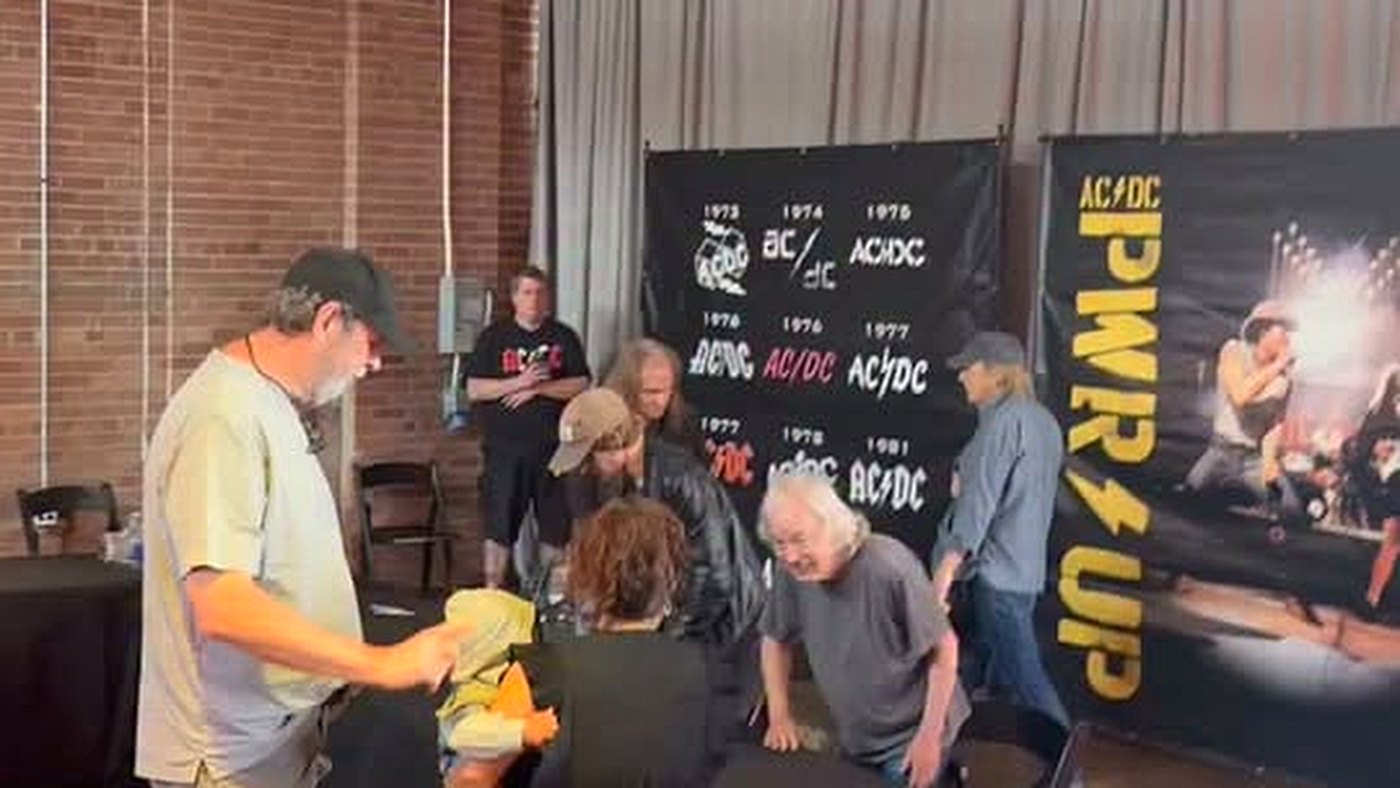 Angus Young autografa um bebê colocado na mesa durante evento do AC/DC em Toronto