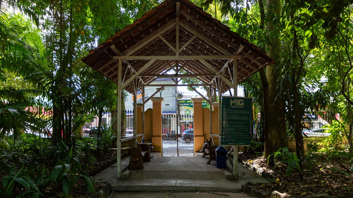 Pavilhão de madeira coberto, no meio de árvores, marca a entrada de um caminho no Parque Zoobotânico do Museu Goeldi em Belém