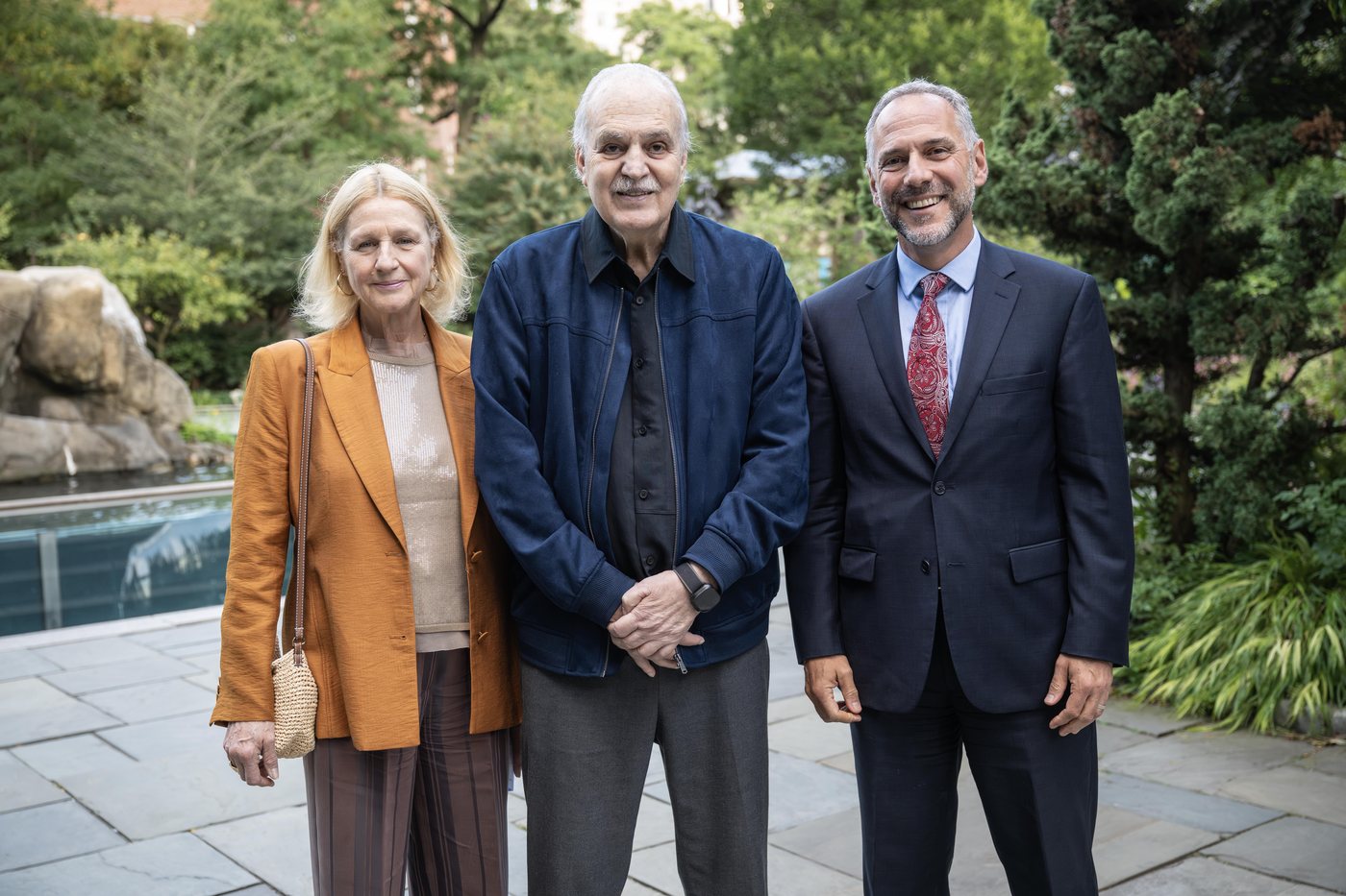 Carlos Nobre entre a mulher, Anna Amelia Costa, de blazer laranja, e Adam Falk, de terno, num jardim do Zoológico do Central Park