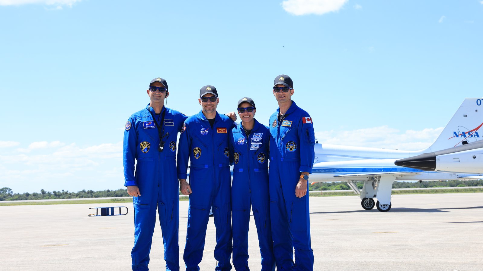 Os quatro tripulantes da Crew-13 de macacão azul posando na pista do Centro Espacial Kennedy, na Flórida, com um jato T-38 da NASA ao fundo