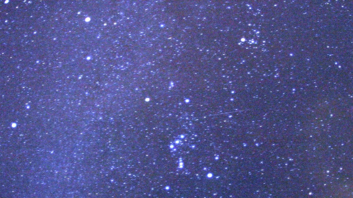 Céu estrelado com a Via Láctea e um risco fino de meteoro Orionídea cruzando a parte de baixo da imagem