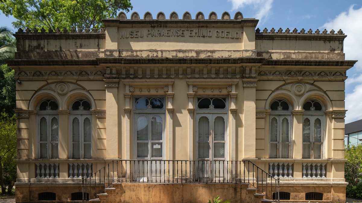 Fachada de prédio histórico bege com o nome Museu Paraense Emílio Goeldi no alto, janelas em arco e balaustrada, em Belém