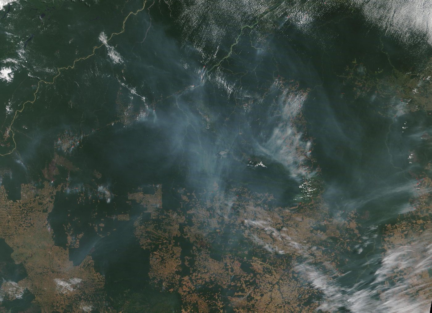 Imagem de satélite da Amazônia brasileira com floresta verde escura, áreas desmatadas marrons e um véu de fumaça cinza sobre a região