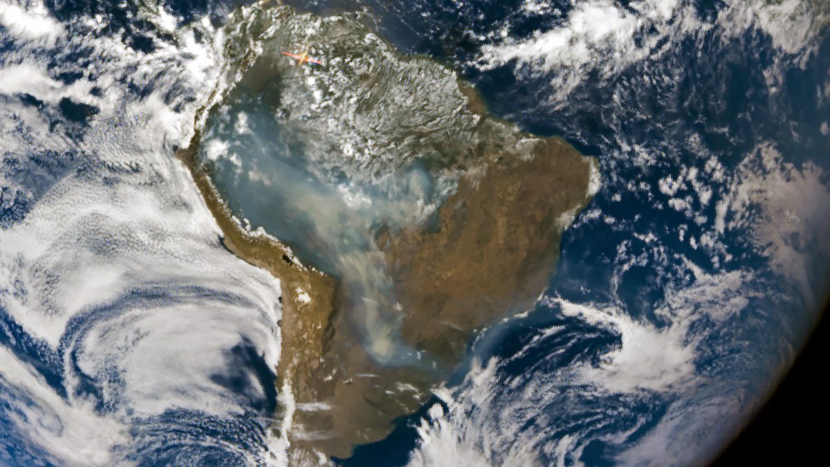Planeta Terra visto do espaço com uma mancha cinza de fumaça de queimadas sobre o centro da América do Sul