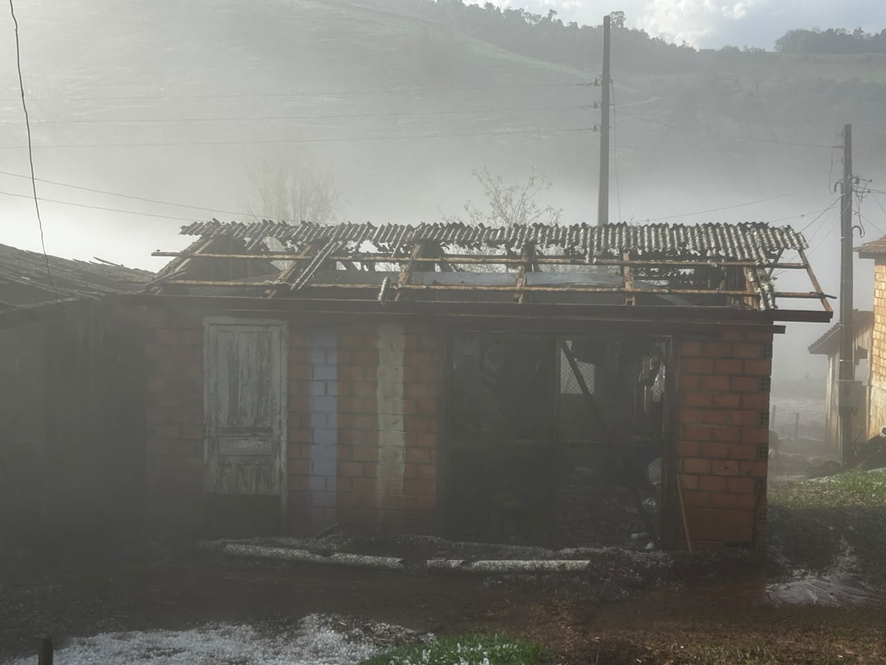 Casa de tijolos com o telhado destruído pelo granizo no Oeste de Santa Catarina, com pedras de gelo no chão
