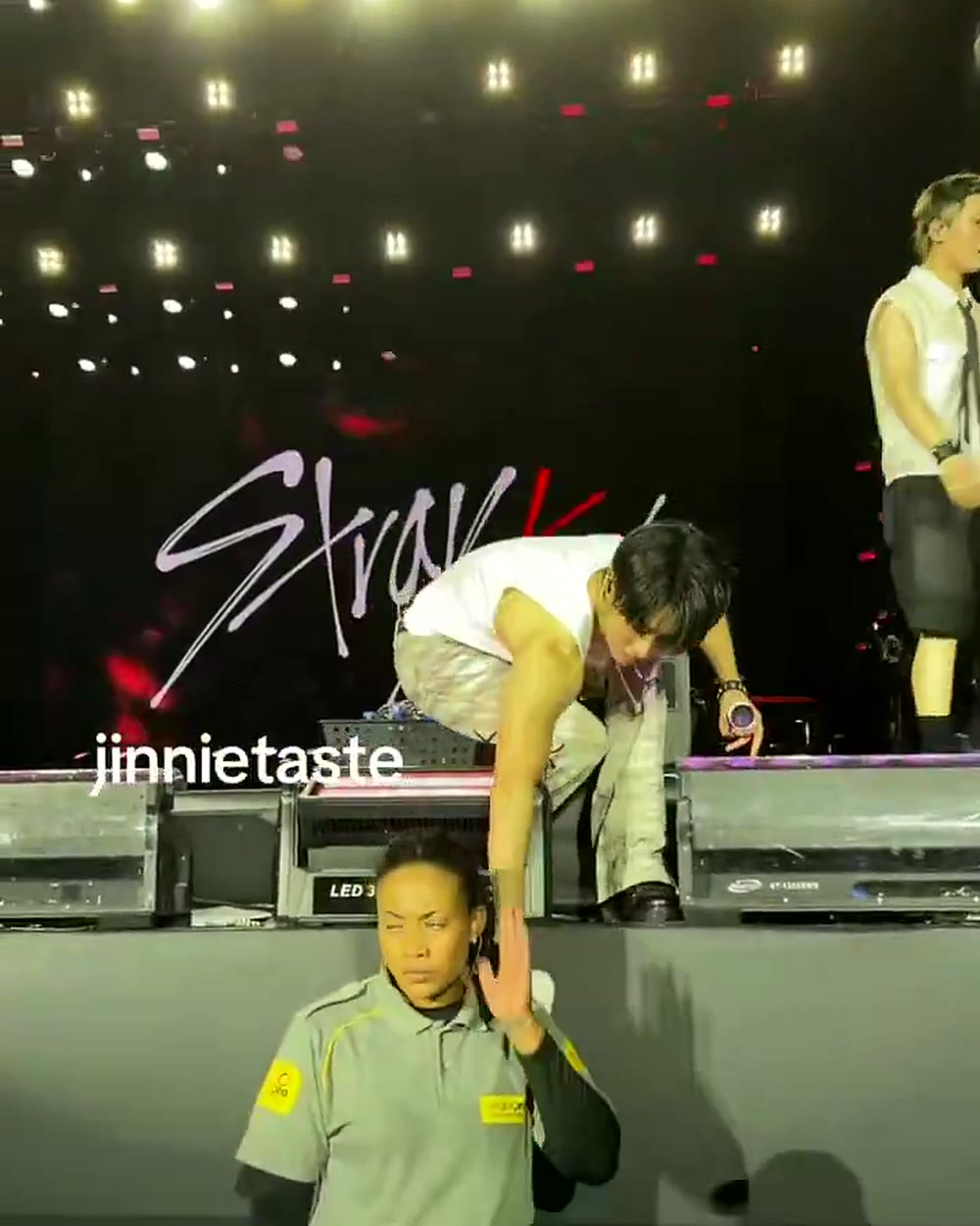 Jisung se abaixa no palco para pegar a toalha antes de descer até a segurança