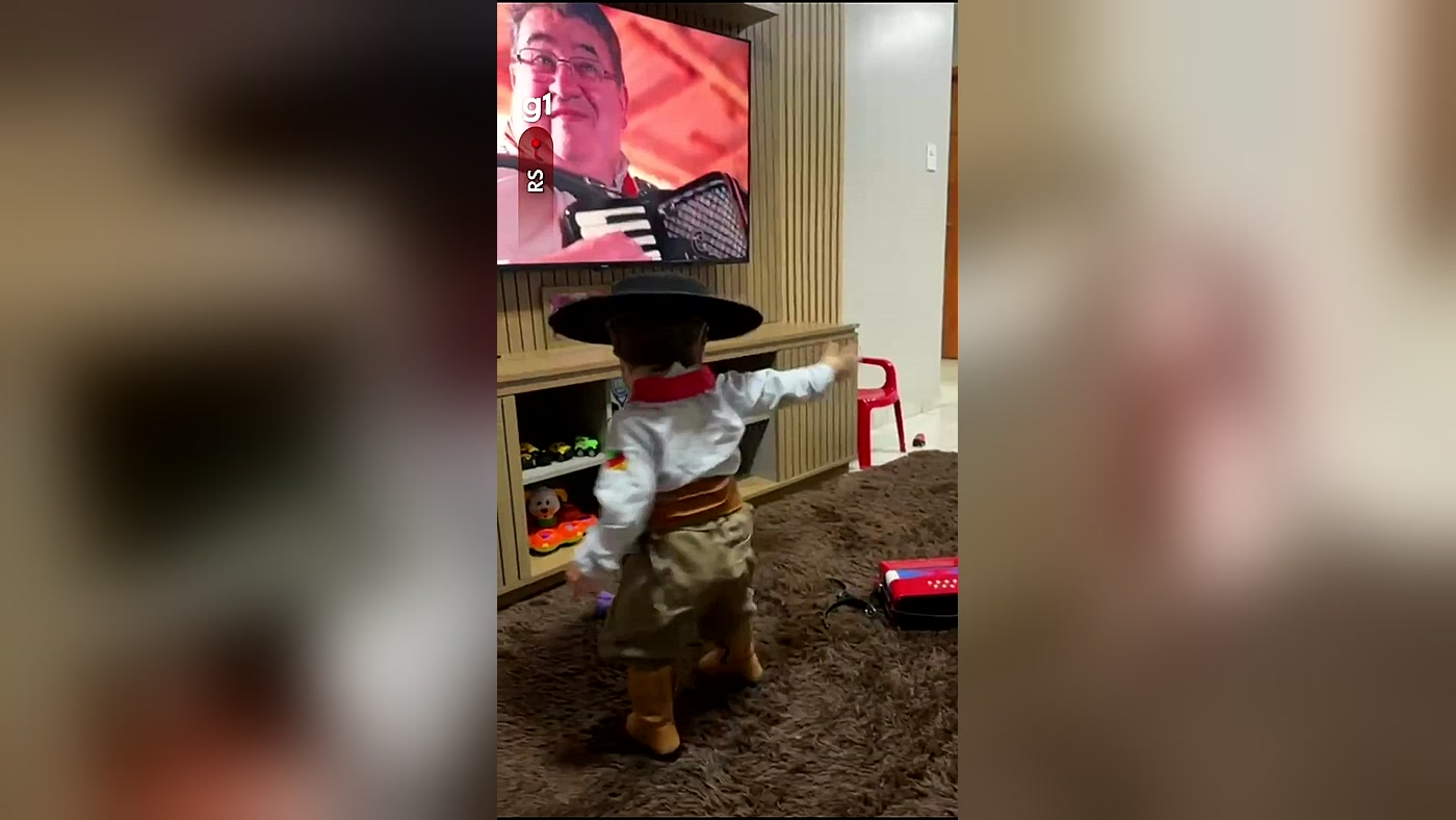 Joaquim, de pilcha e chapéu, dançando de costas em frente à TV, em cena do vídeo do g1 RS