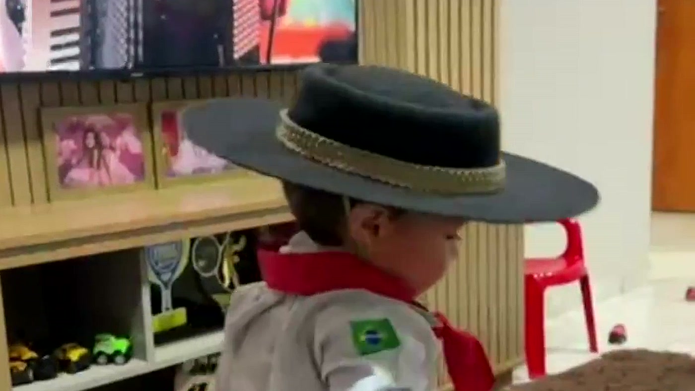 Joaquim, de 1 ano e 3 meses, dançando música gaúcha de pilcha e chapéu na sala, em frame do vídeo do g1