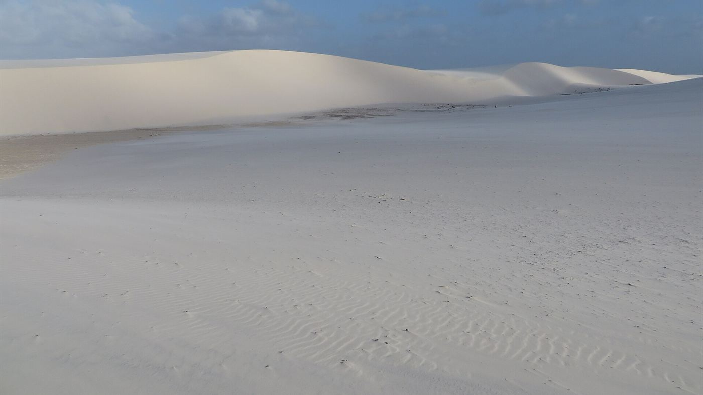 Duna de areia branca esculpida pelo vento nos Lençóis Maranhenses, com marcas onduladas na superfície da areia.
