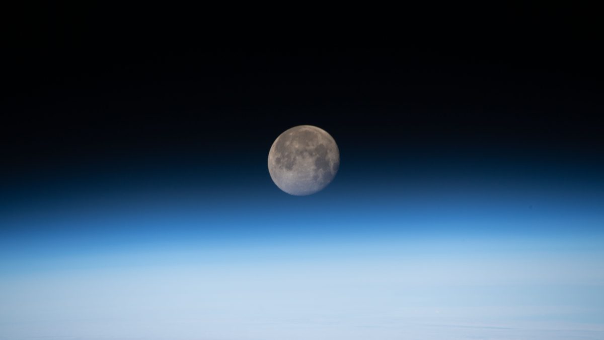 Lua gibosa minguante, quase cheia, com as crateras visíveis, acima do horizonte azul da Terra visto da Estação Espacial