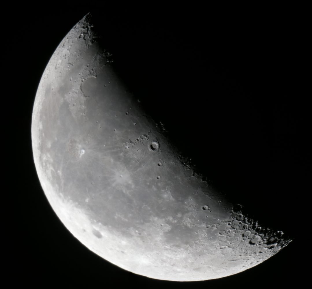 Lua minguante com crateras e o lado iluminado voltado para a esquerda, sobre fundo preto, fotografada por telescópio