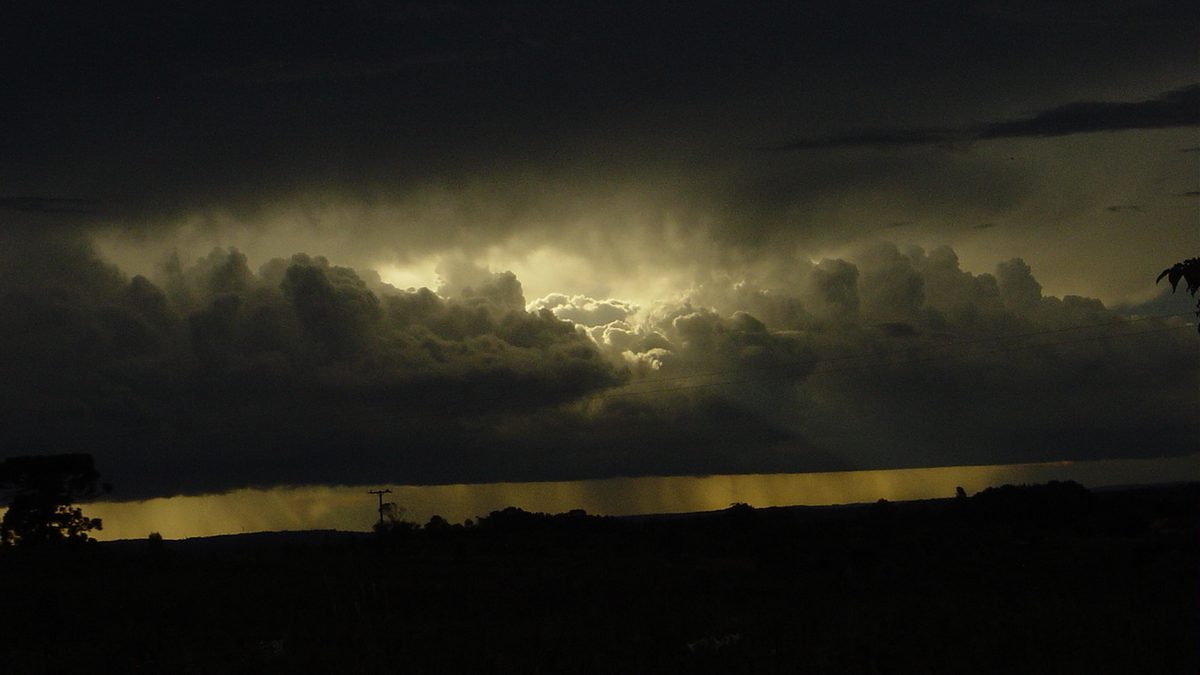 Nuvem de tempestade escura com cortina de chuva ao fundo e luz amarelada no horizonte, na Lapa, no Paraná