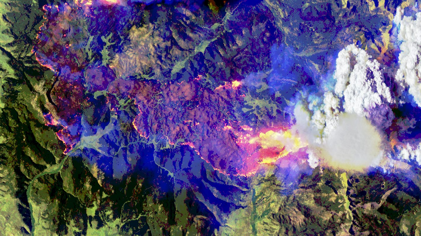 Mesma cena do incêndio Sand Creek em cores falsas com infravermelho: fogo ativo em rosa e amarelo, área queimada em marrom, nuvens em branco e fumaça em azul e roxo