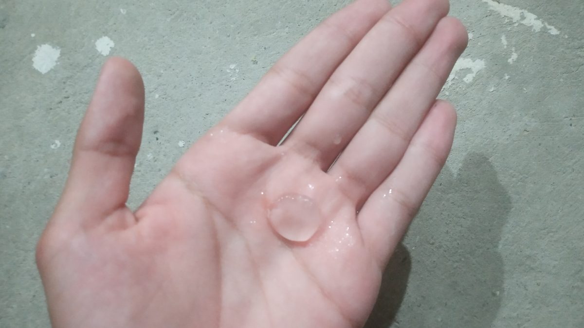 Palma de uma mão com uma única pedra de granizo transparente do tamanho de uma moeda, sobre piso de cimento