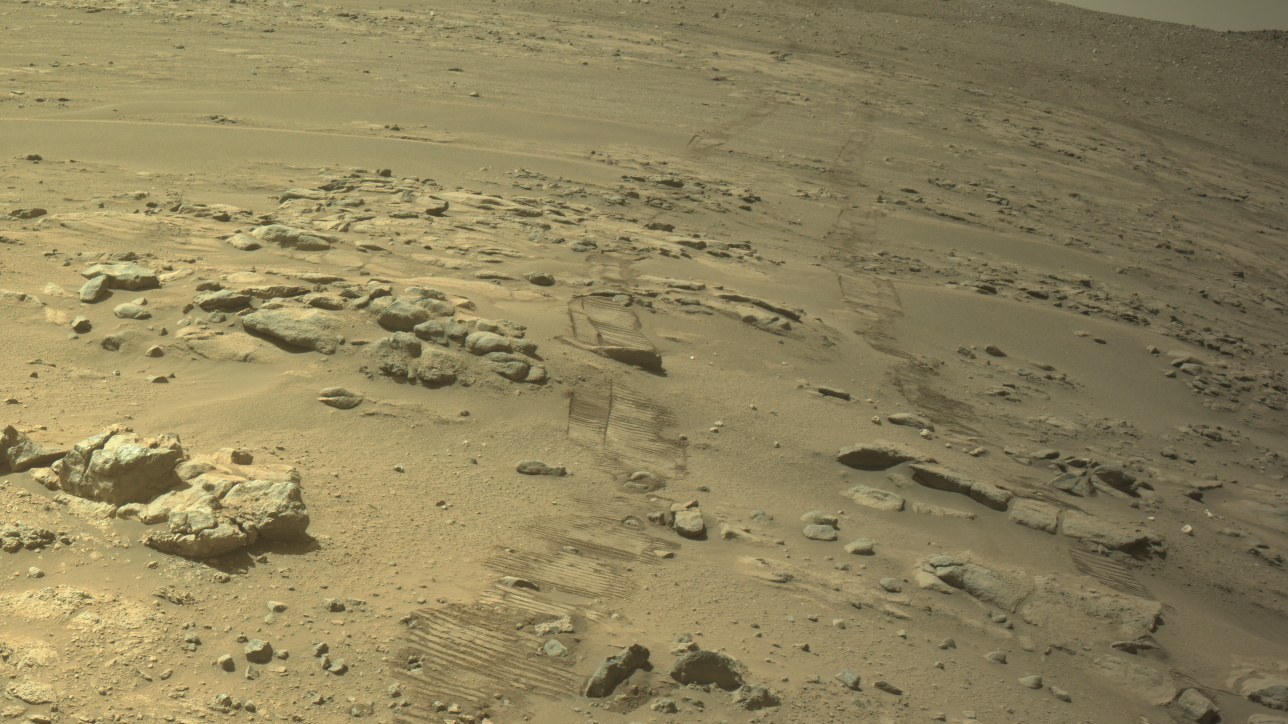 Solo avermelhado de Marte com rochas e as marcas das rodas do rover cruzando a imagem, vistas pela câmera de navegação em que o Perseverance bate recorde