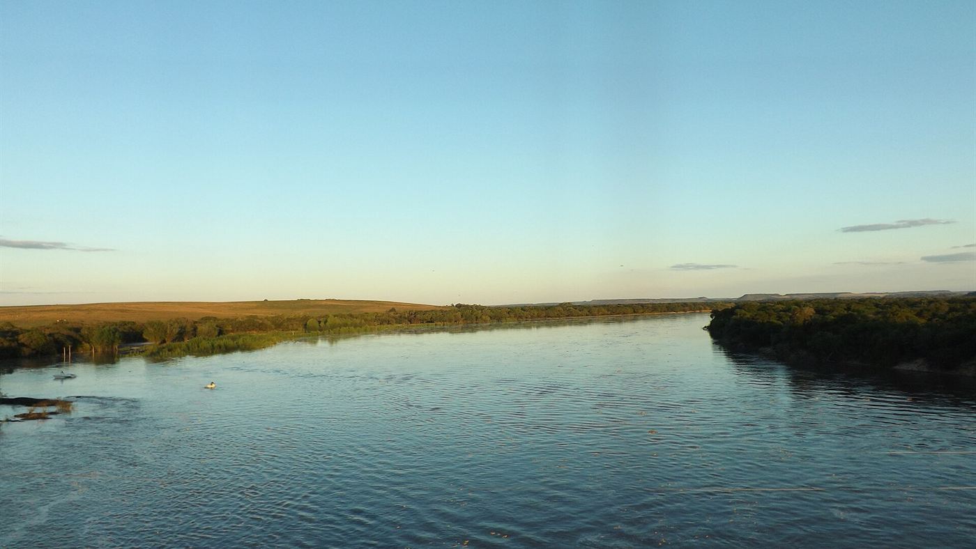 Rio Ibicuí, largo e calmo, com mata ciliar nas margens e campo ao fundo, no Rio Grande do Sul