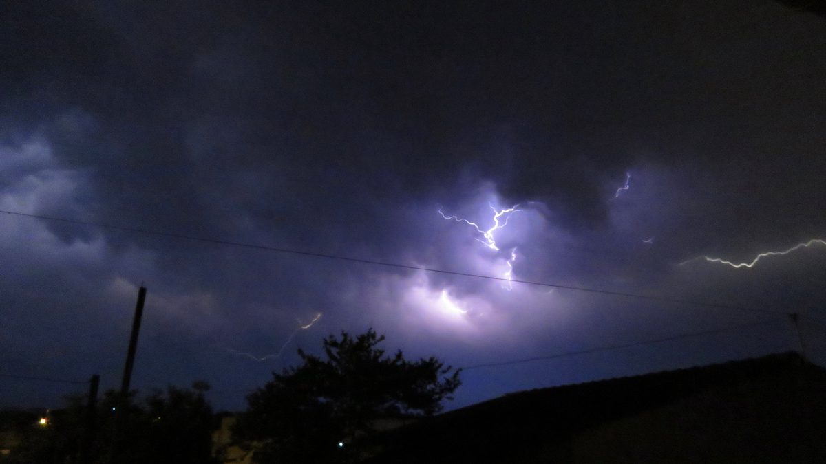 Raios riscam nuvens escuras sobre fios e telhados numa noite de temporal em Viamão, no Rio Grande do Sul