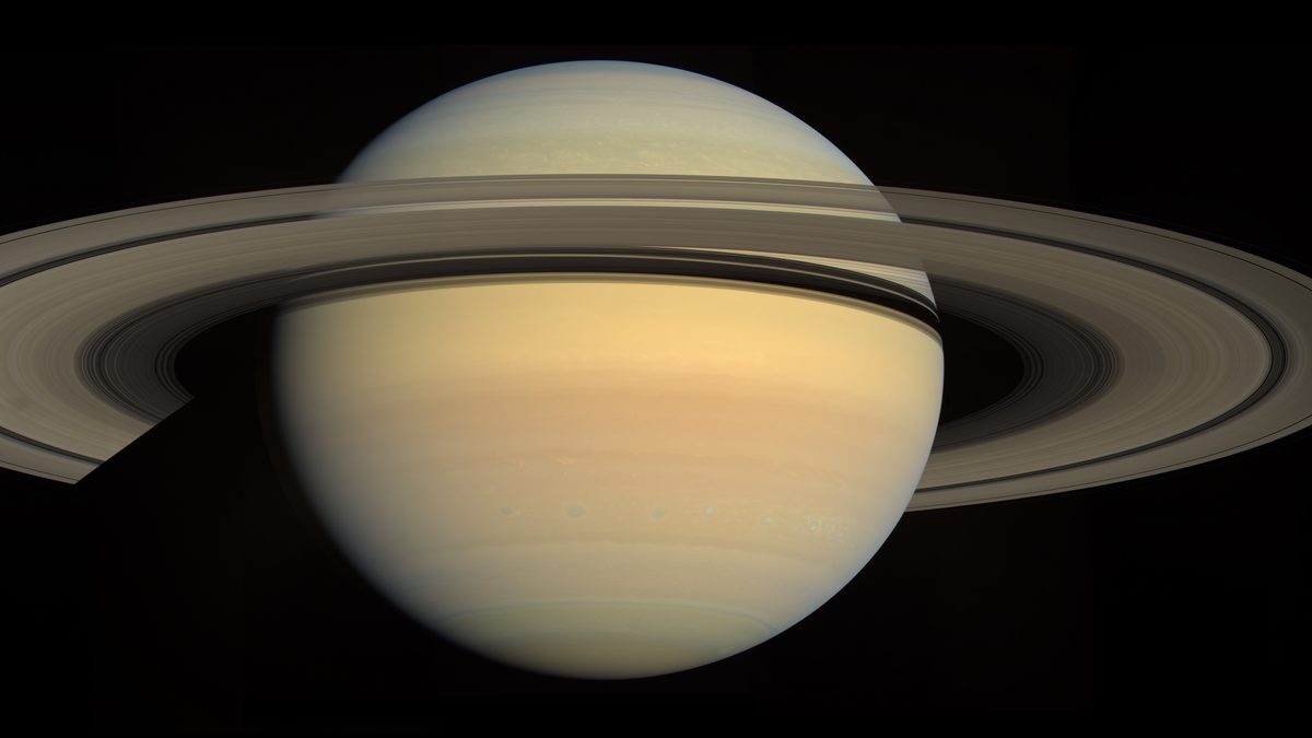Saturno com os anéis abertos em mosaico de imagens da sonda Cassini, mostrando as faixas amareladas do planeta e a sombra dos anéis
