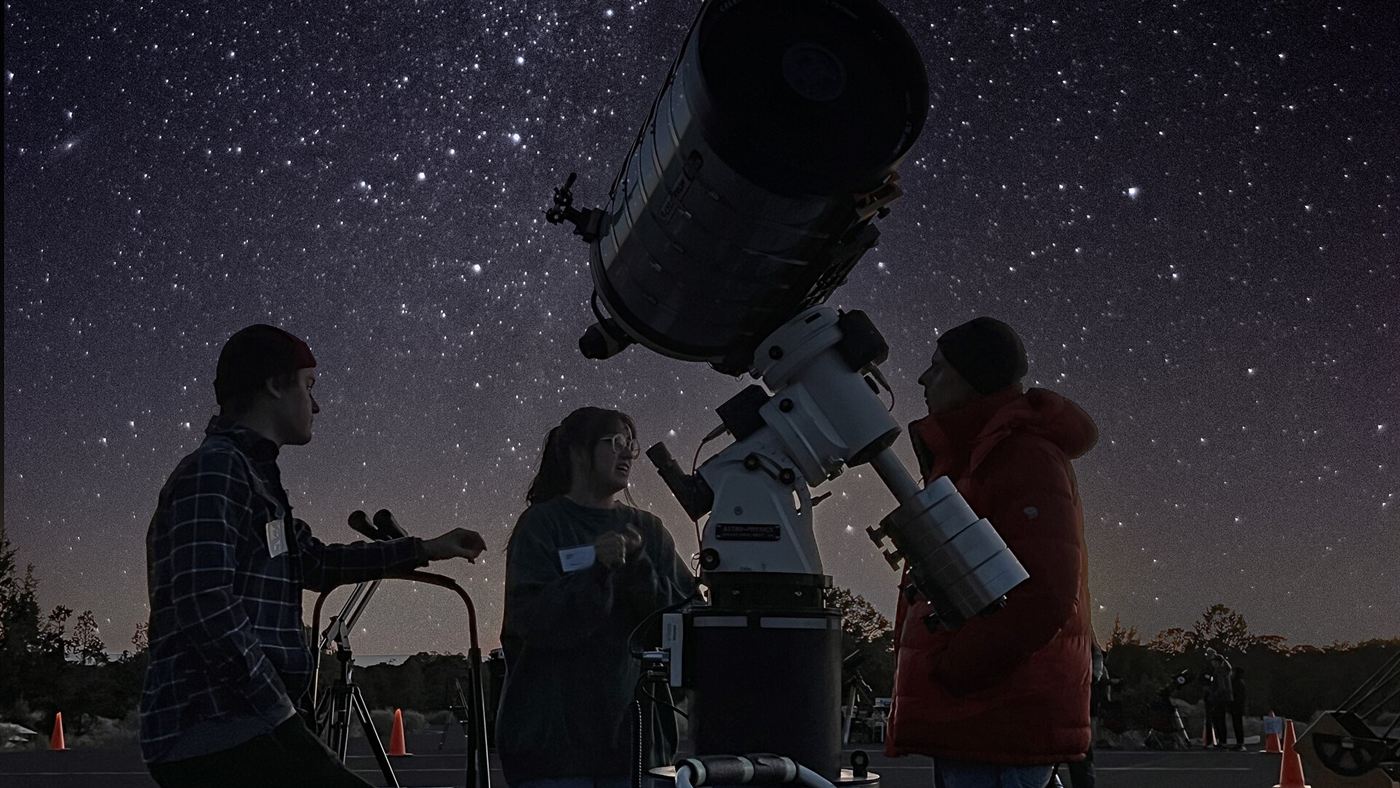 grupo observa o céu estrelado com um telescópio grande durante evento de astronomia amadora.