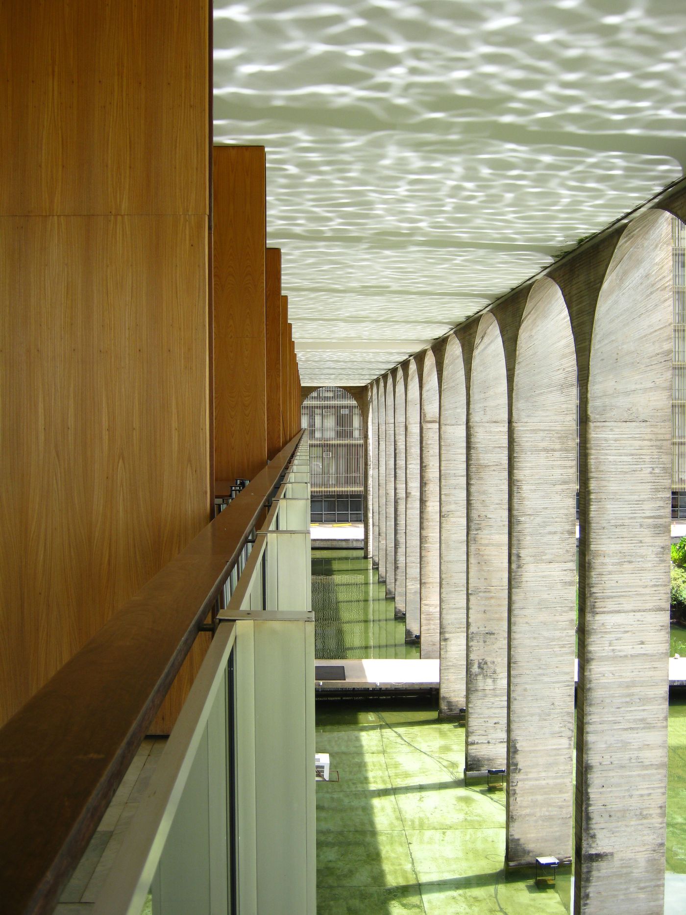 Arcos do Palácio do Itamaraty vistos da varanda, com a água esverdeada do espelho d'água embaixo e o reflexo da água no teto da marquise