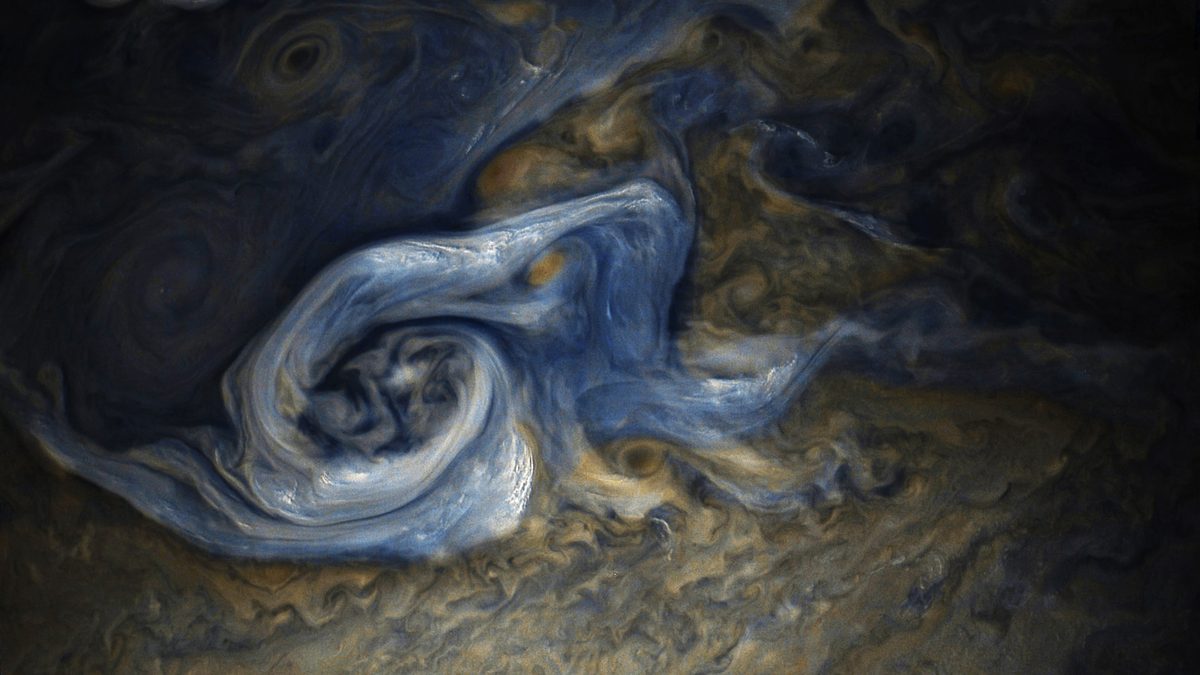 Tempestade em espiral de nuvens azuladas e alaranjadas no hemisfério norte de Júpiter, em imagem de cores realçadas da sonda Juno