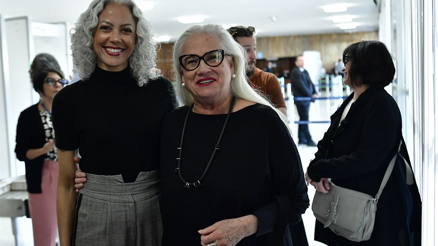 Vera Holtz sorri ao lado de outra mulher em corredor